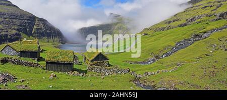 Panorama du village de Saksun avec de vieilles maisons de ferme traditionnelle à bforeground Pollurin, Laguna est à l'arrière-plan, l'île de Streymoy féroïen Banque D'Images