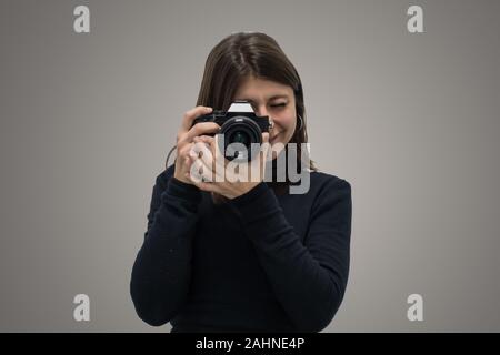 Jolie fille de race blanche élégante de prendre une photo avec appareil photo mirrorless isolé sur fond gris. Concept d'élégance en photographie Banque D'Images