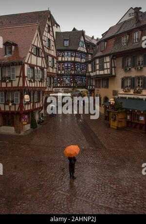 Personne avec un parapluie orange debout dans la pluie à l'extérieur de la Maison des Douanes, Colmar, France Banque D'Images