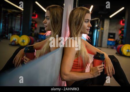 Jeune jolie femme se reposant dans une salle de sport après l'exercice Banque D'Images