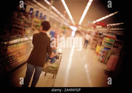 Vue arrière d'une femme poussant son bébé dans un panier à l'intérieur d'un supermarché. Banque D'Images