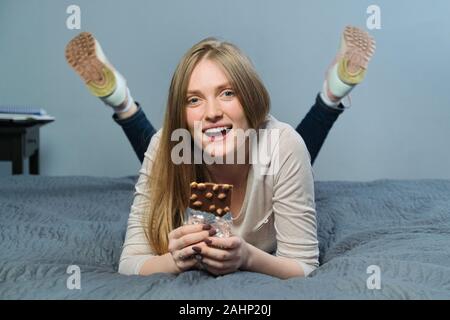 Belle jeune femme souriante avec le chocolat. Le chocolat au lait avec noisettes dans les mains de happy girl lying on the bed Banque D'Images