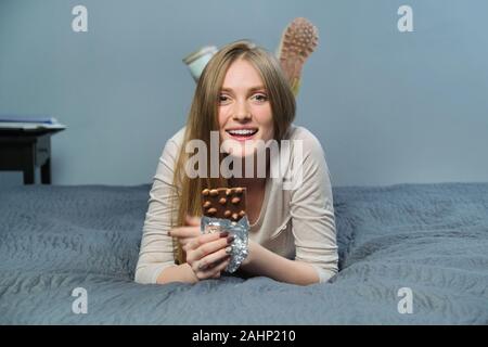 Belle jeune femme souriante avec le chocolat. Le chocolat au lait avec noisettes dans les mains de happy girl lying on the bed Banque D'Images