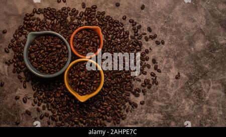 Les grains de café organiques Matières premières fraîches dans un grand nombre de tasses colorées avec des tailles différentes éparpillées sur un comptoir d'ardoise Banque D'Images