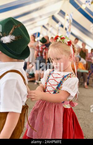 Une jeune fille mignonne en robe dirndl tenant des jarretelles de son frère à Oktoberfest à New Glarus, Wisconsin, États-Unis Banque D'Images