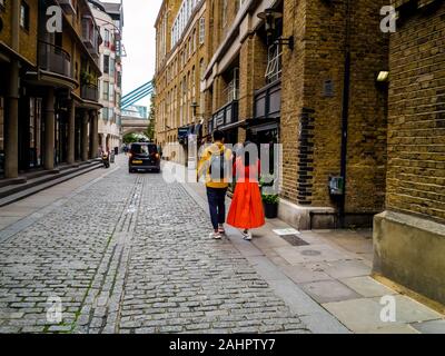 Quelques touristes se promènent le long d'une rue londonienne près du Tower Bridge, Royaume-Uni Banque D'Images