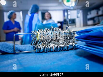 Hemostats alignés sur transporteur en salle d'opération avec les professionnels de la diffusion dans l'arrière-plan Banque D'Images