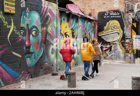 Femme et enfants passant street art et graffiti peint sur l'extérieur des bâtiments dans le quartier de La Candelaria de Bogota, Colombie Banque D'Images