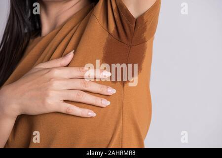 Gros plan femme asiatique avec l'hyperhidrose la transpiration. Jeune femme d'Asie de sueur tache sur ses vêtements contre un arrière-plan gris. Concept de soins de santé. Banque D'Images