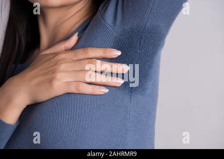 Gros plan femme asiatique avec l'hyperhidrose la transpiration. Jeune femme d'Asie de sueur tache sur ses vêtements contre un arrière-plan gris. Concept de soins de santé. Banque D'Images