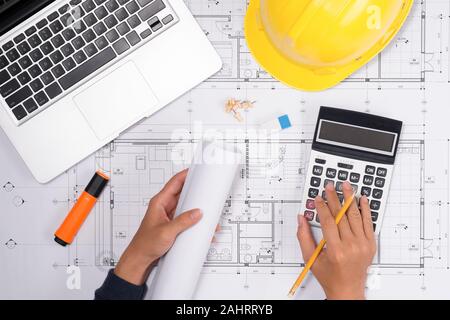 Main sur les plans de construction avec casque jaune et outils de dessin sur les bleus Banque D'Images