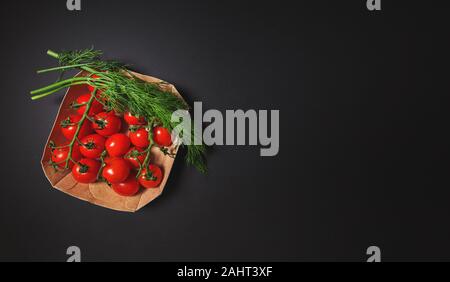 Tomates cerises rouges avec de l'aneth sur un fond noir dans une boîte en carton. Banque D'Images