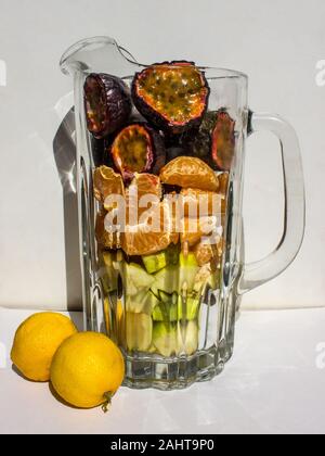 Différents type de coupe de fruits, notamment des fruits de la Passion, mandarines et pommes dans une tasse en verre sur un fond blanc. Banque D'Images
