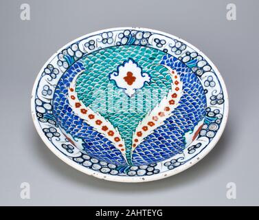 Islamique. Plat (Tabaq) avec écailles et feuilles dentelées. 1550-1599. La Turquie. Fritware avec peinture sous glaçure en bleu, turquoise, rouge, noir et le centre de conception de ce plat est doté de deux lames opposées entourant un centre de trois lobes (trèfle) forme, tous les poissons sur un motif à grande échelle dans des tons turquoise et bleu. La conception des feuilles est dans le soi-disant style saz (Reed), se référant à la reed plume utilisée par des artistes turcs et persans pour créer des dessins à l'encre noire. Premiers dessins dans ce style dépeignent dragons et phénix en combat entouré de fleurs et plumes-comme des feuilles. La jante o Banque D'Images