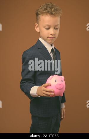 Portrait de jeune garçon comme businessman wearing poursuite contre fond brun Banque D'Images