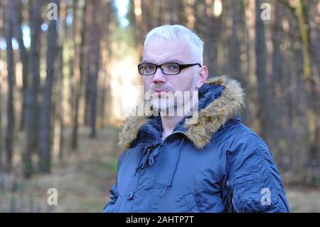 Closeup portrait d'un homme intelligent avec les cheveux gris et des lunettes, une barbe dans l'hiver au chaud dans le contexte de la forêt. Surprise. Banque D'Images