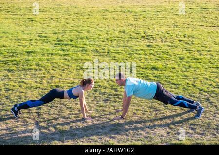 Jeune couple de mettre en place les sportifs boy and girl doing exercise sur l'herbe verte de l'extérieur du stade. Banque D'Images