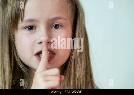 Close-up portrait of little child girl with long hairholding pointer du doigt à ses lèvres en silence. Banque D'Images