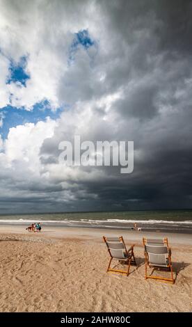 Deux transats abandonnés en face de nuages noirs orageux sur St Augustine Beach, Floride USA Banque D'Images