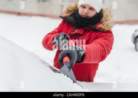 L'homme en rouge avec capuche fourrure manteau d'hiver voiture nettoyage après la tempête de neige Banque D'Images