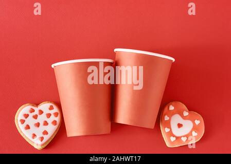 Les cookies en forme de coeur décorée et deux tasses à café en papier sur fond rouge. Valentines Day food concept Banque D'Images