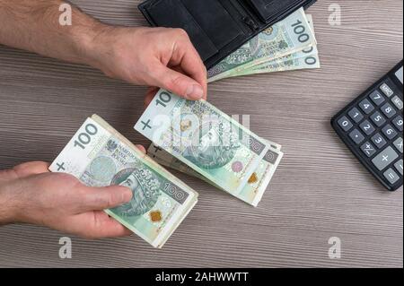 Les mains d'hommes comptant Polish zloty billets tableau ci-dessus avec un porte-monnaie et calculatrice Banque D'Images