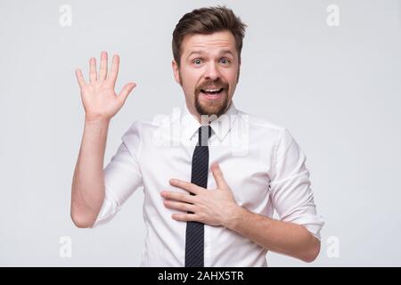 Young caucasian man in white shirt jurant avec les mains sur la poitrine et ouvrez palm, faire une promesse de fidélité Banque D'Images