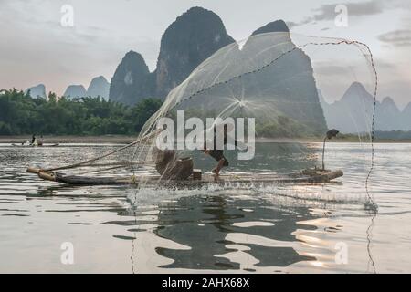 Pêcheur cormorant au coucher du soleil jetant un filet circulaire en fonte, Li River près de Xingping, Guangxi, Chine Banque D'Images