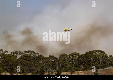 Vol en hélicoptère Bell 412 contre les panaches de fumée pendant la lutte contre les feux de brousse dans la région de Victoria, en Australie. Banque D'Images