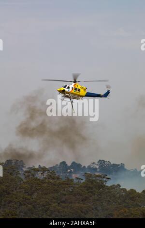 Vol en hélicoptère Bell 412 contre les panaches de fumée pendant la lutte contre les feux de brousse dans la région de Victoria, en Australie. Banque D'Images