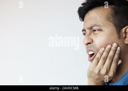 Un jeune homme tenant le menton inférieur dans la douleur et l'agonie en raison de maux isolés en blanc avec copie espace pour le texte Banque D'Images