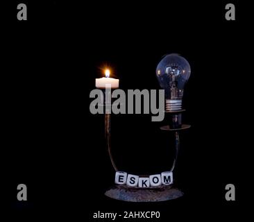 Un bougeoir avec une ampoule électrique et une bougie allumée avec le terme Eskom isolé sur fond noir image en format horizontal Banque D'Images