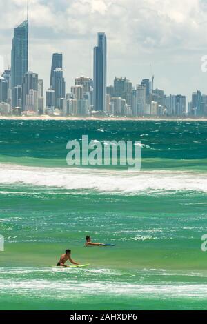 Gold Coast, Australie - Février 21, 2016 : Deux jeunes surfeurs sur le surf boards dans de l'eau avec la ville de Gold Coast skyline sur l'arrière-plan Banque D'Images