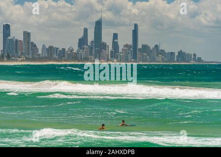 Gold Coast, Australie - Février 21, 2016 : Deux jeunes surfeurs sur le surf boards dans de l'eau avec la ville de Gold Coast skyline sur l'arrière-plan Banque D'Images