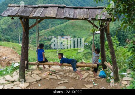 Cat Cat, le Vietnam - 20 août 2017 : les enfants vietnamiens jouer sur bambou swing avec terrasses de riz de montagne dans l'arrière-plan Banque D'Images