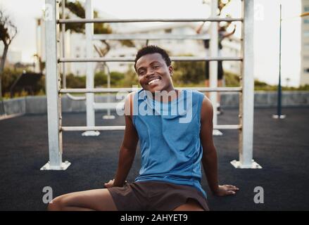 Portrait of a smiling young african american male sportif relaxant après entraînement intensif dans la salle de sport en plein air park Banque D'Images