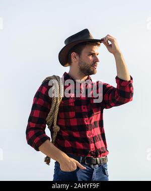 Ranch travailleur. La vie au ranch. Cowboy avec lasso corde fond de ciel. Eco farm. Concept de l'agriculture. Bel homme en chapeau et costume de style rustique. Garder ranch. Agriculteur réfléchie réflexion sur l'entreprise. Banque D'Images