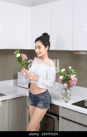 Young Asian woman arranging flowers dans la cuisine. Banque D'Images