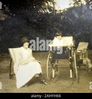 Old vintage photographie en noir et blanc d'une femme était assise dans un transat à côté d'un landau avec un bébé assis dans elle, dans un jardin Banque D'Images