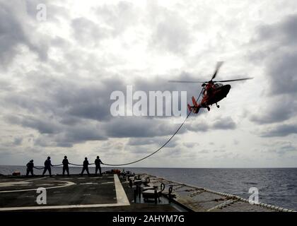 Un équipage de la Garde côtière des États-Unis à bord d'un hélicoptère MH-65 Dolphin effectue un ravitaillement en vol en hélicoptère (HIFR) avec garde-Bertholf (WMSL 750) de l'équipage tandis que les patrouilles de la faucheuse la mer des Philippines, le 12 avril 2019. Les opérations de formation des équipages HIFR pour transférer le carburant tout en gardant l'hélicoptère en vol au cas où l'hélicoptère ne peuvent pas atterrir sur l'outil de coupe en raison de mauvais état de la mer, les défaillances mécaniques, occupé un poste de pilotage ou d'autres raisons, ils ne peuvent pas la terre. U.S. Coast Guard photo de Maître de 1re classe Matthew S. Masaschi. Banque D'Images