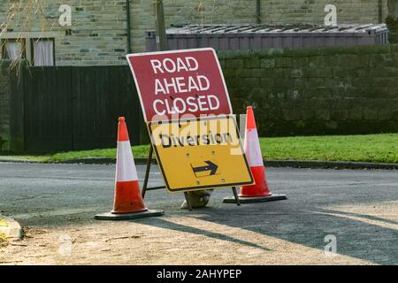 Une fermeture de route rouge signe (UK) au milieu de cônes de signalisation rouge et blanc. Un détournement jaune signe est en dessous. Banque D'Images