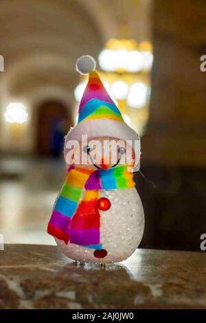 Petit bonhomme portant un foulard et un chapeau arc-en-ciel contre une lumière dorée bokeh en attente de l'époque de Noël et cadeaux Banque D'Images