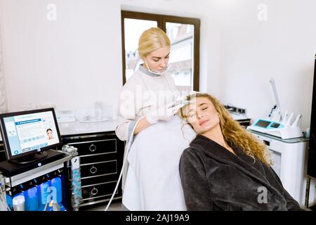 Jeune femme médecin-cosmetologist rend la procédure de microdermabrasion la peau du visage d'une belle et jeune femme en cosmétologie clinique. Professi Banque D'Images