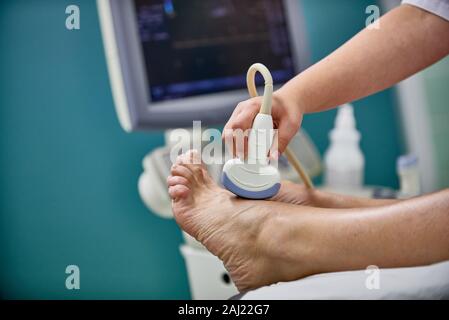 Médecin avec l'appareil d'échographie dans une main checkst pied de patient Banque D'Images