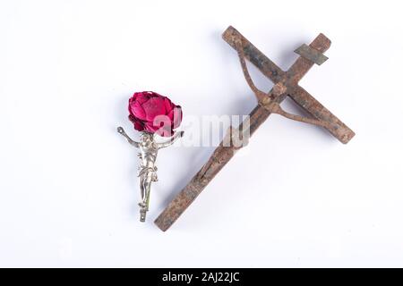 Christ en métal argenté sur fond blanc avec rose rose derrière elle à côté de rusty metal crucifix où le Christ est fait d'ongles Banque D'Images