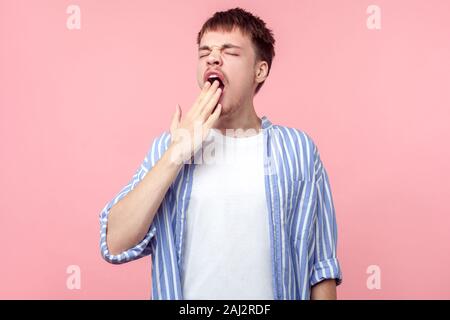 Portrait d'homme fatigué endormi étudiant ou travailleur occasionnel dans le bâillement chemise rayée et couvrant la bouche avec la main, souffrant de manque de sommeil, l'épuisement Banque D'Images