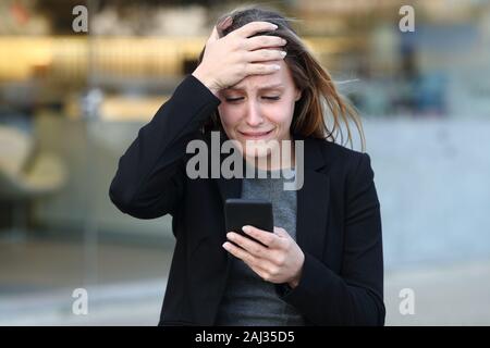 Vue de face d'une triste plainte exécutif contrôle smart phone dans la rue à côté d'office Banque D'Images
