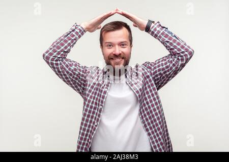 Portrait de satisfait heureux homme barbu en chemise à carreaux décontractée faisant symbole de la chambre, le toit sur la tête et de sourire, se sentir en sécurité, protégé 09/12/2012 10 Banque D'Images