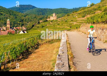Jeune femme à vélo sur route le long des Vignes de Riquewihr à Kaysersberg village, Alsace, France Banque D'Images