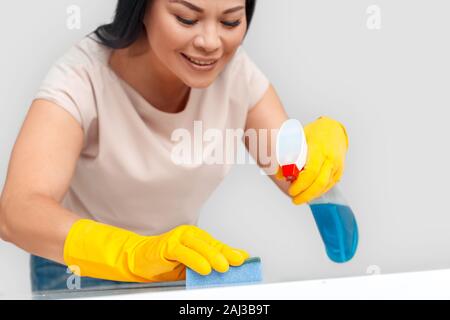 Femme Asiatique portant des gants de caoutchouc article isolé sur fond blanc holding spray cleaning surface de la table avec éponge smiling concentrés close-up Banque D'Images